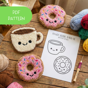A pink frosted donut with colorful sprinkles and a smiling coffee cup punch needle coaster set, placed on a rustic wooden table next to a real cup of latte