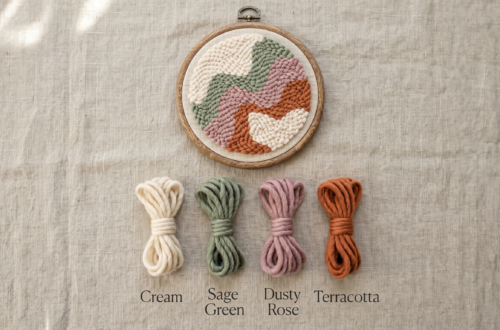 Wooden embroidery hoop containing abstract punch needle piece in cream, sage green, dusty rose, and terracotta, with four yarn threads displayed below labeled with color names