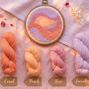Punch needle template and color palette inspiration for nursery decor. A completed abstract sunset hoop art is displayed with matching labeled yarn skeins (Coral, Peach, Rose, Lavender) on a soft pink background