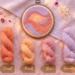 Punch needle template and color palette inspiration for nursery decor. A completed abstract sunset hoop art is displayed with matching labeled yarn skeins (Coral, Peach, Rose, Lavender) on a soft pink background